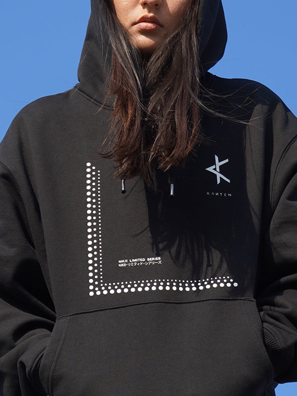 Person wearing a black hoodie with white text and graphics against a blue sky