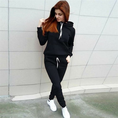 Person wearing a black hoodie and pants with white sneakers against a tiled wall.